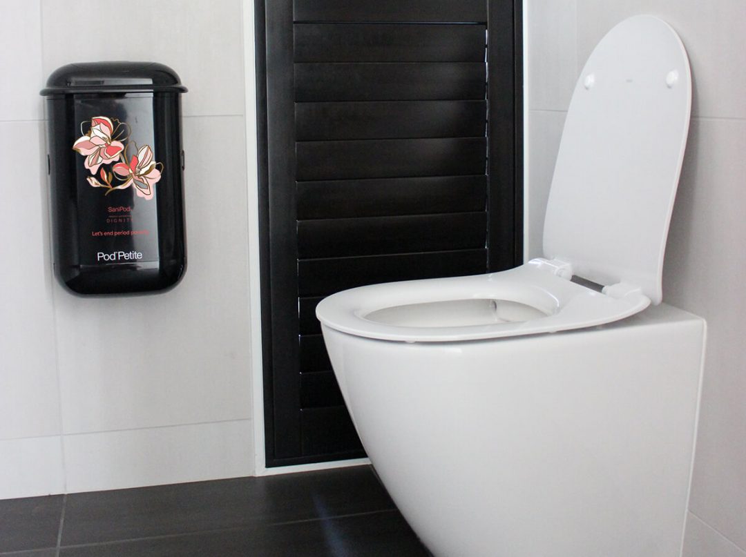 A black Pod Petite sanitary disposal unit beside a toilet with a Pod Wrap SaniPod x Dignity decal.