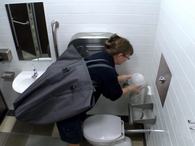 A hygiene service technician servicing a SaniPod in a washroom
