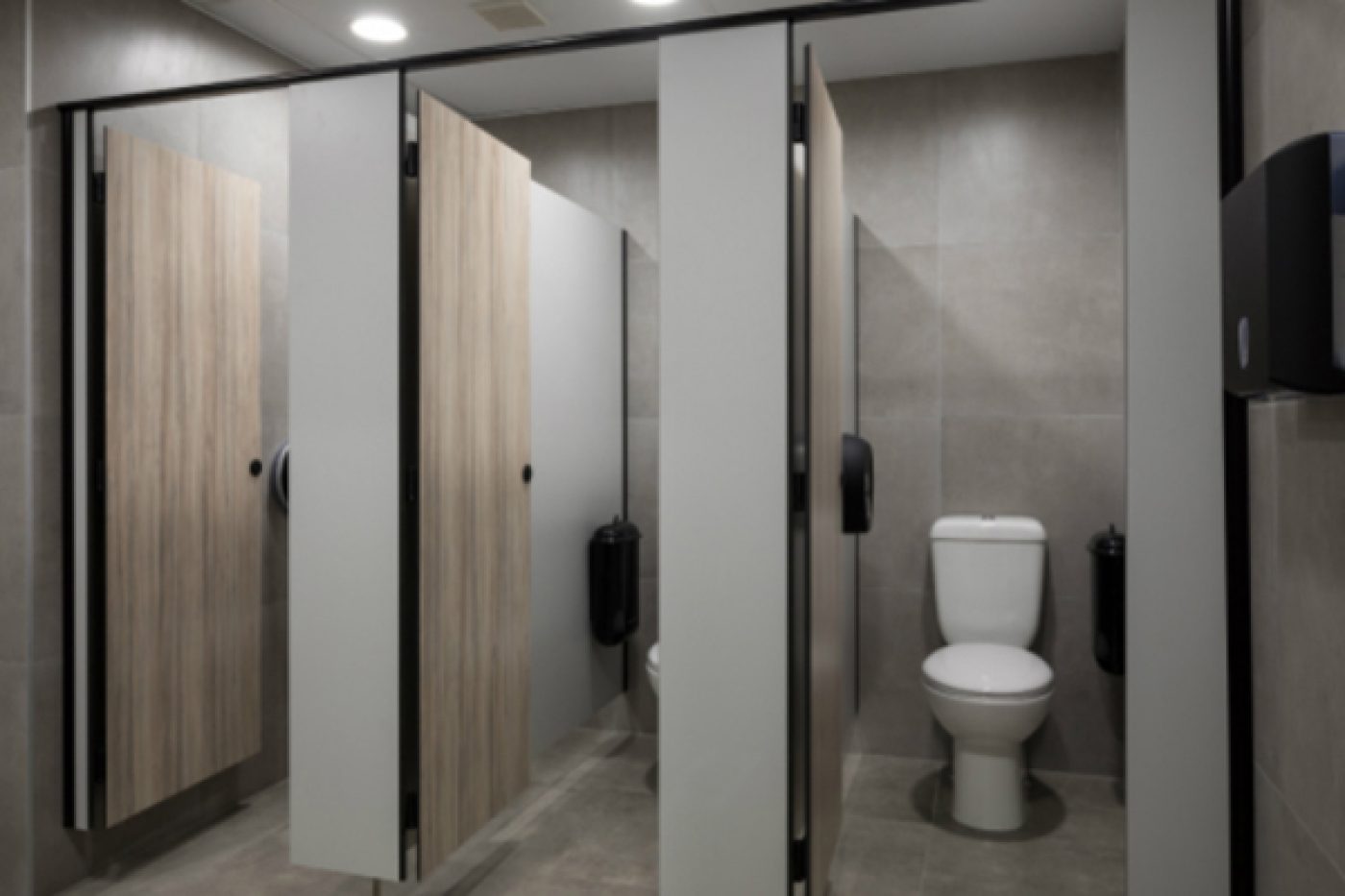 Restroom cubicles featuring black Pod Petite manual units installed in side wall