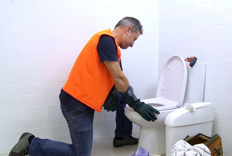 Plumber fixing blocked toilet caused by flushed sanitary waste