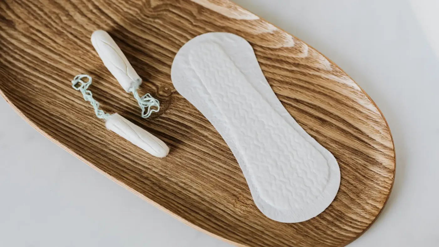 Tampon vs pad – flatlay of tampon and pad on wooden tray illustrating feminine hygiene