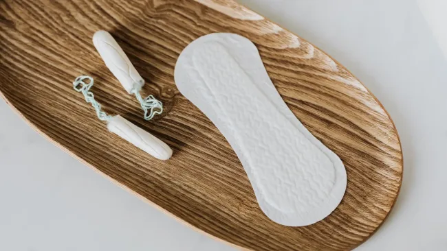 Tampon vs pad – flatlay of tampon and pad on wooden tray illustrating feminine hygiene