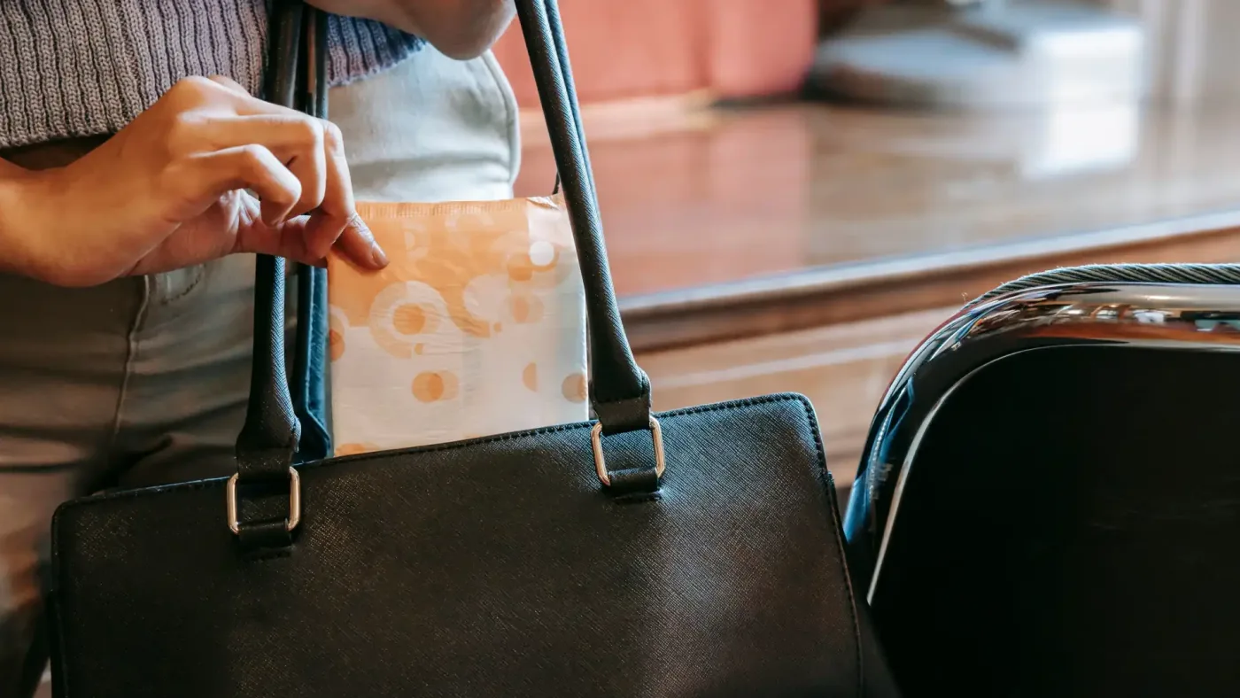 free period products at work – woman discretely places a sanitary pad into a black handbag