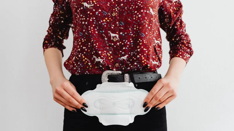 period products - woman in a colorful shirt holds a sanitary pad, symbolising menstrual health awareness
